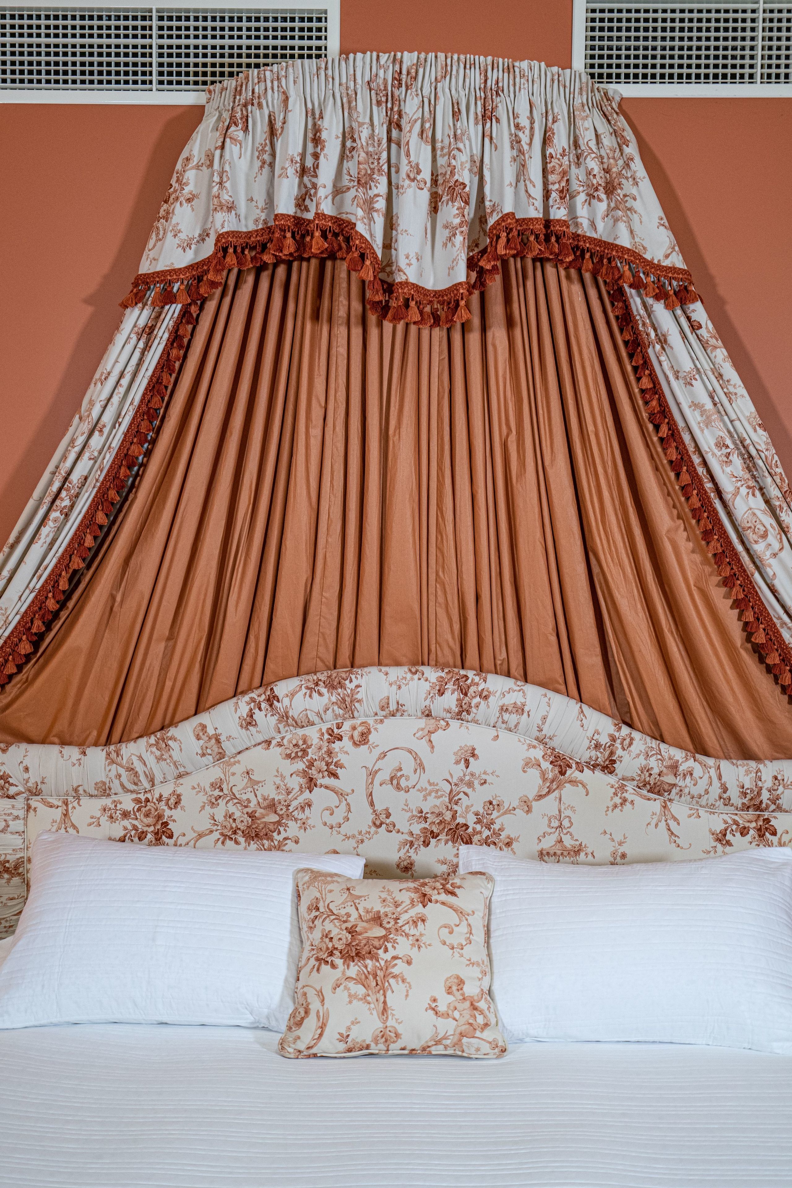 A bed with a canopy, pillows, and a headboard with floral patterns.