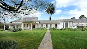 Une grande maison blanche de style colonial, avec un chemin de pierre menant à l’entrée, entourée de pelouses bien entretenues et d’un palmier.