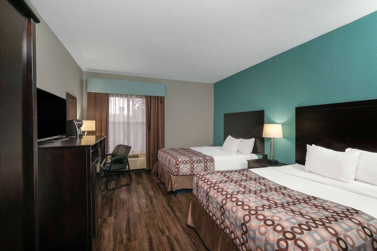 Una camera d'albergo con due letti, una scrivania, una sedia, una televisione e una finestra con tende.
