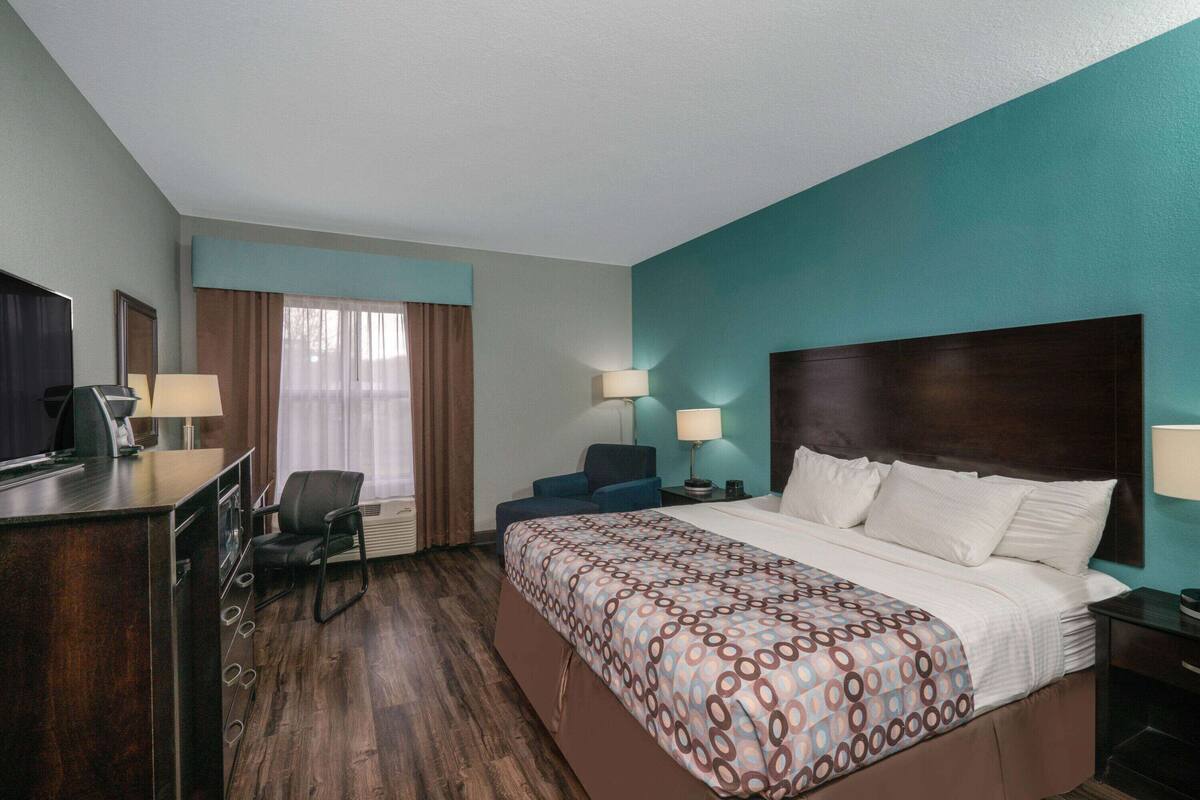 Una camera d'albergo con un letto, una scrivania, una sedia, una televisione e una finestra con tende.