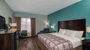 Habitación de hotel con cama, escritorio, silla, televisor y ventana con cortinas.