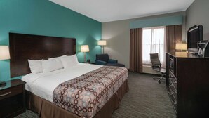 A hotel room with a large bed, two bedside tables with lamps, a desk with a chair, a television, and a window with curtains.