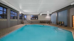 An indoor swimming pool with a clear view of the pool area, a staircase, and seating arrangements.