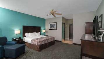 A hotel room with a bed, a desk, a chair, a desk lamp, a nightstand, a wall-mounted TV, and a ceiling fan.