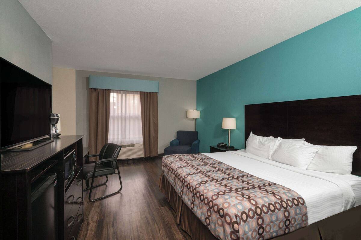 Una camera d'albergo con un letto, una scrivania con televisore, una sedia e una finestra con tende.