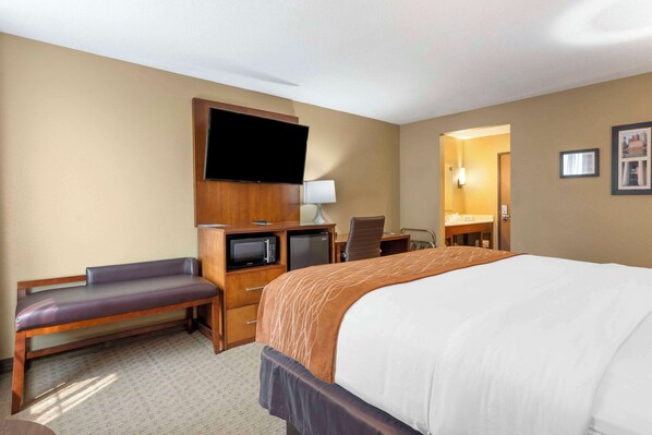 A hotel room with a bed, a desk, a chair, a television, a microwave, and a bathroom visible through an open door.