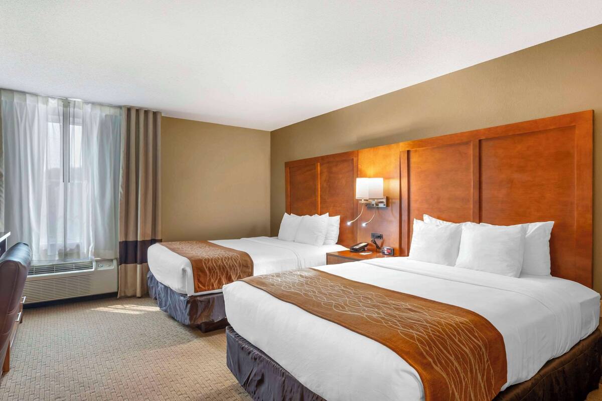 A hotel room with two beds, a desk, a chair, a lamp, and a window with curtains.
