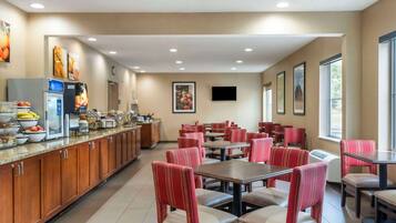 A restaurant with a long counter, red upholstered chairs, and a television mounted on the wall.