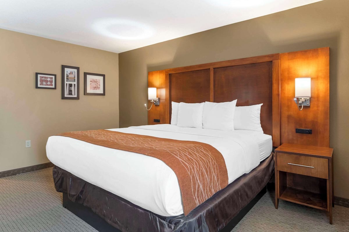 A hotel room with a large bed, wooden headboard, two bedside tables with lamps, and framed pictures on the wall.