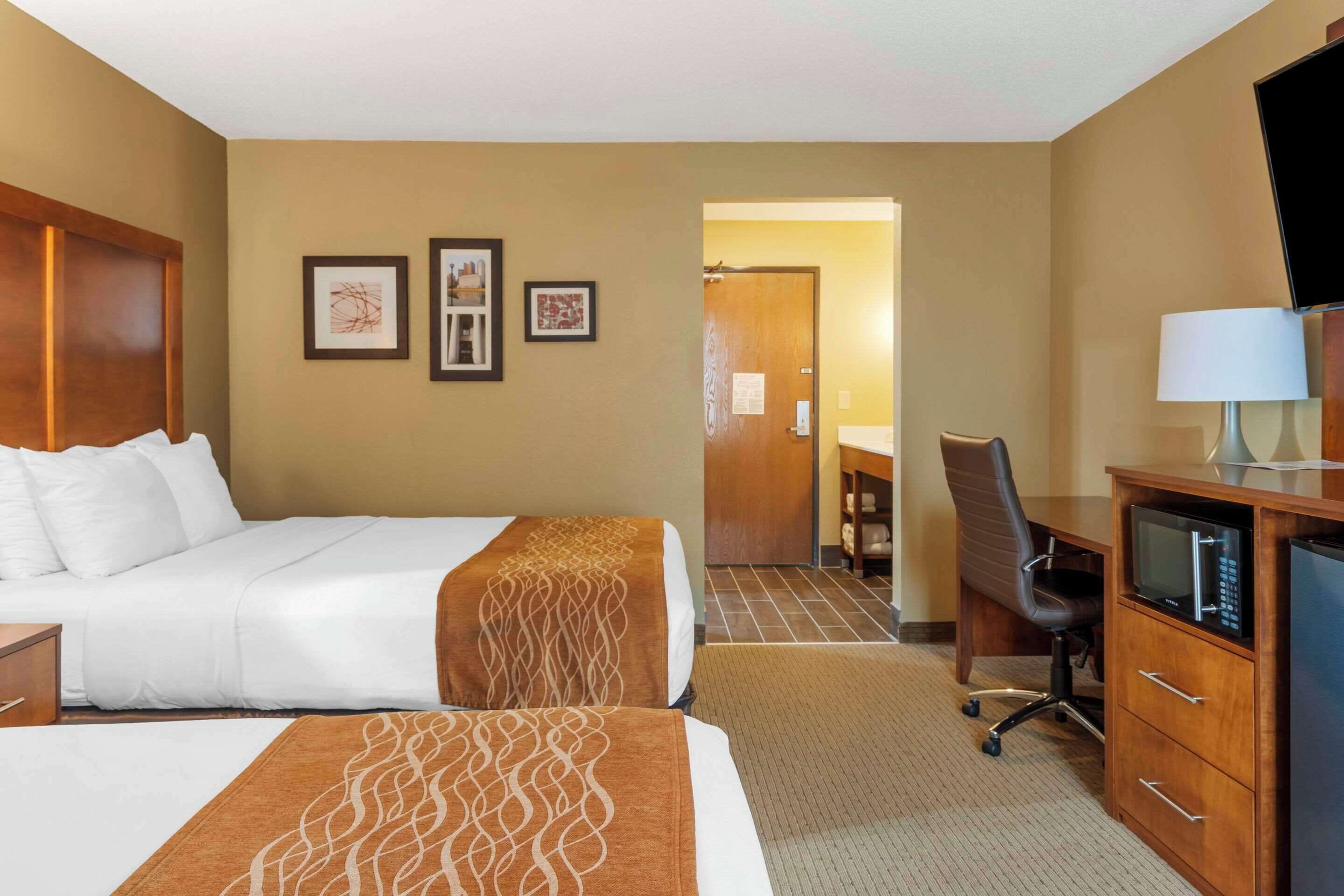 Quarto de hotel com uma cama, uma escrivaninha com computador, televisão e uma cadeira.