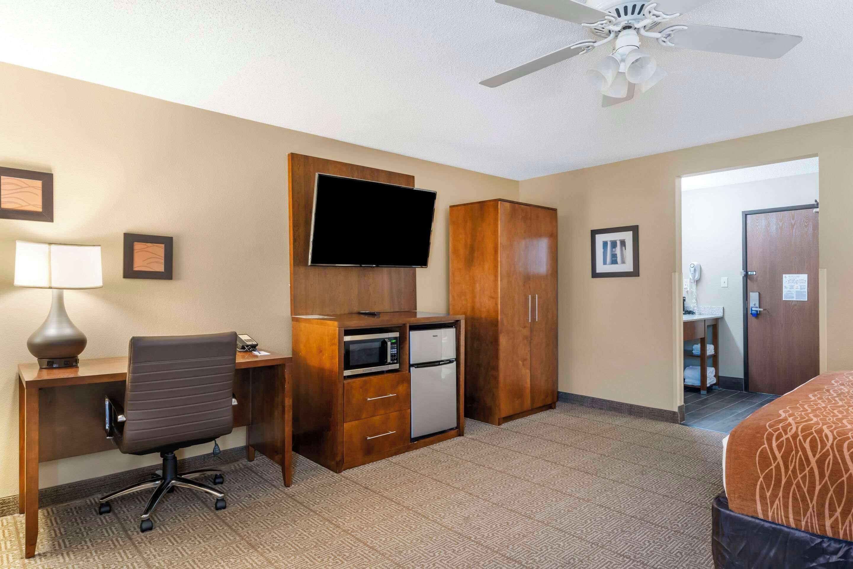 A hotel room with a desk, chair, television, wardrobe, and a bed.
