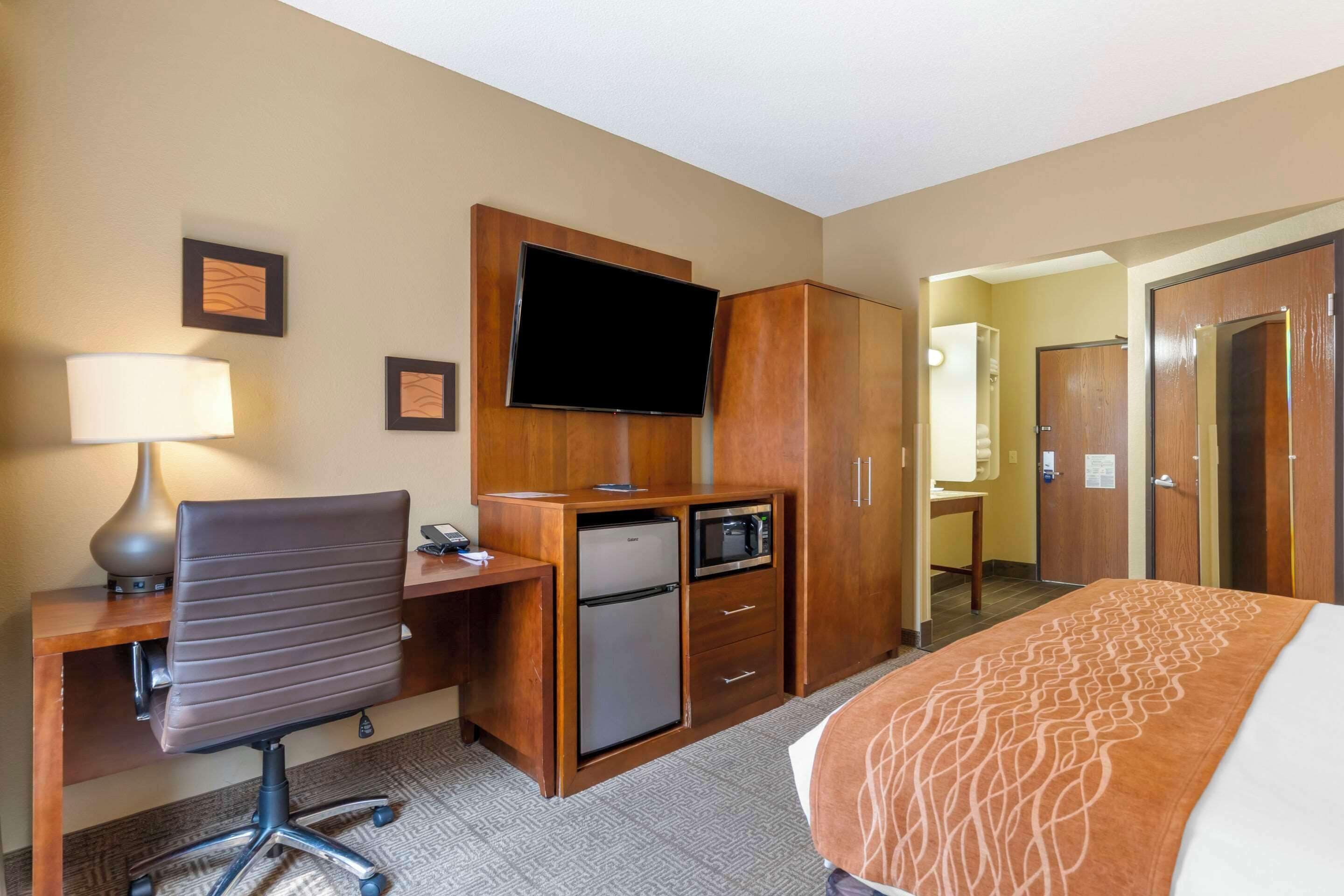 Une chambre d’hôtel équipée d’un lit, d’un bureau, d’une chaise, d’une télévision, d’une armoire et d’un petit réfrigérateur.
