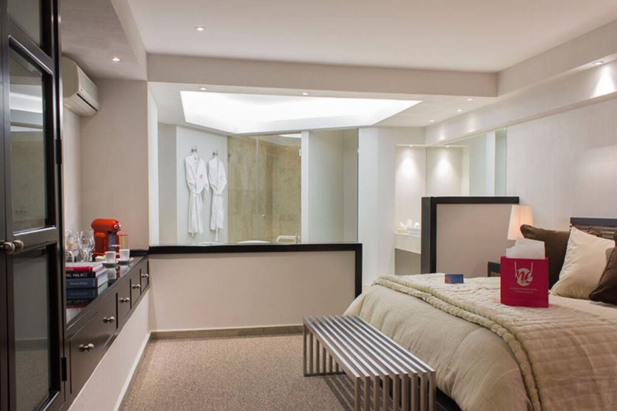 A modern hotel room with a large bed, a bedside table, a mirror, and a window.