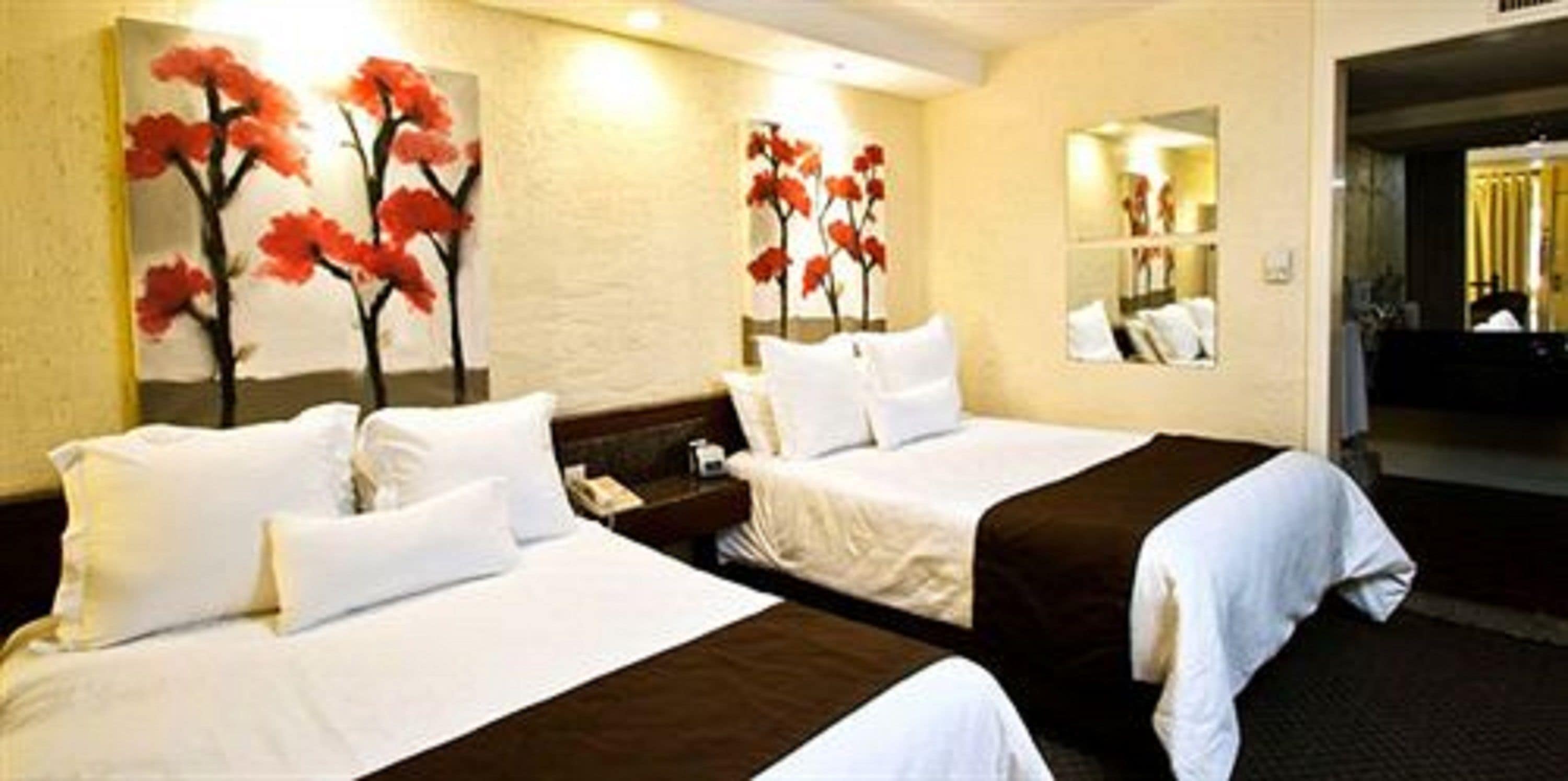 Habitación de hotel con dos camas, ropa de cama blanca y un cuadro de flores rojas en la pared.