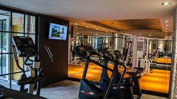 Un gimnasio con máquinas de cardio, equipo de pesas y un espejo grande.