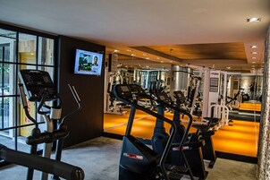 Un gimnasio con máquinas de cardio, equipo de pesas y un espejo grande.