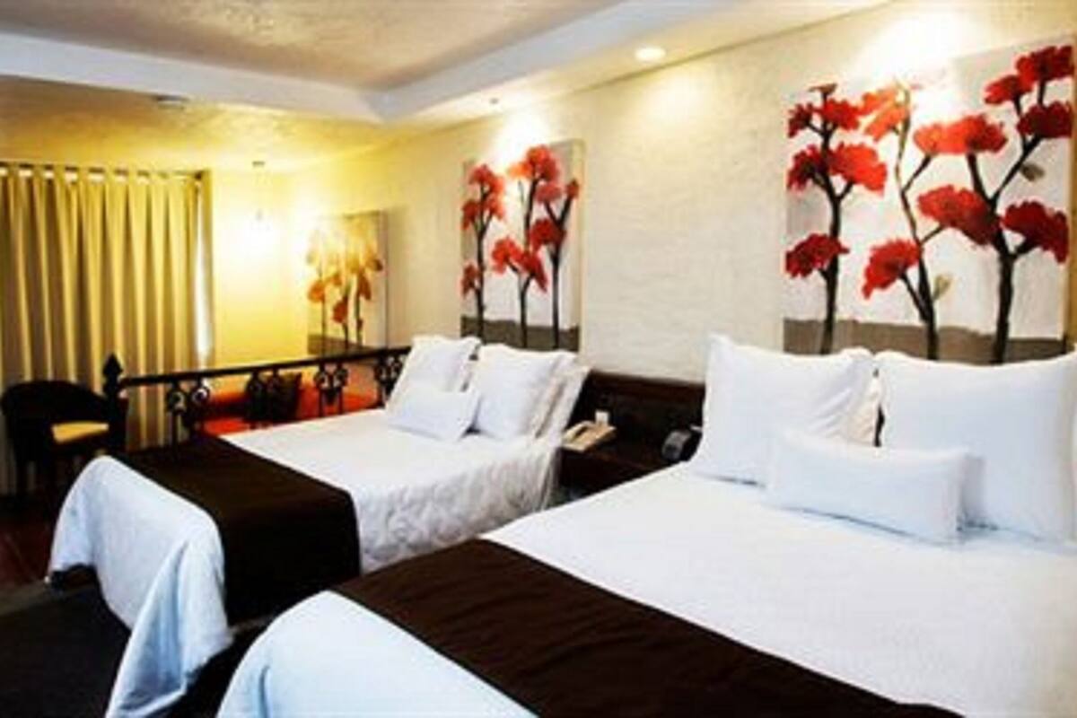 A hotel room with two beds, a desk, and a chair. There are paintings on the wall.