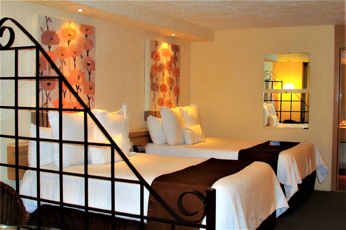 A hotel room with two beds, a large mirror, and floral wall art.