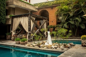 A pool area with a water feature, surrounded by rocks and potted plants. - NEhotel Nueva Estancia (León)