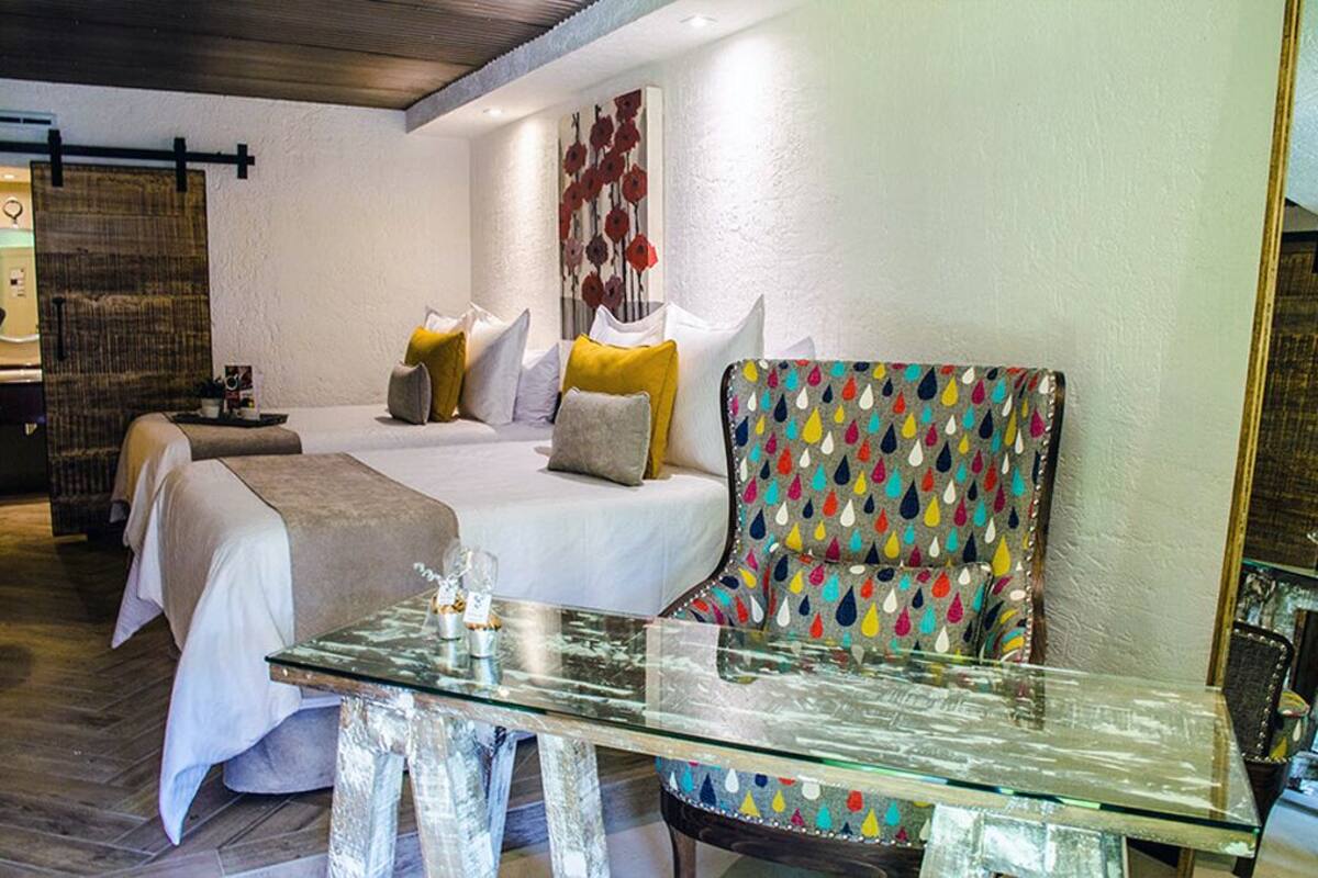 A hotel room with two beds, a glass coffee table, and a colorful chair.