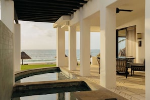 A pool area with a view of the ocean, a thatched umbrella, and a seating area with chairs.