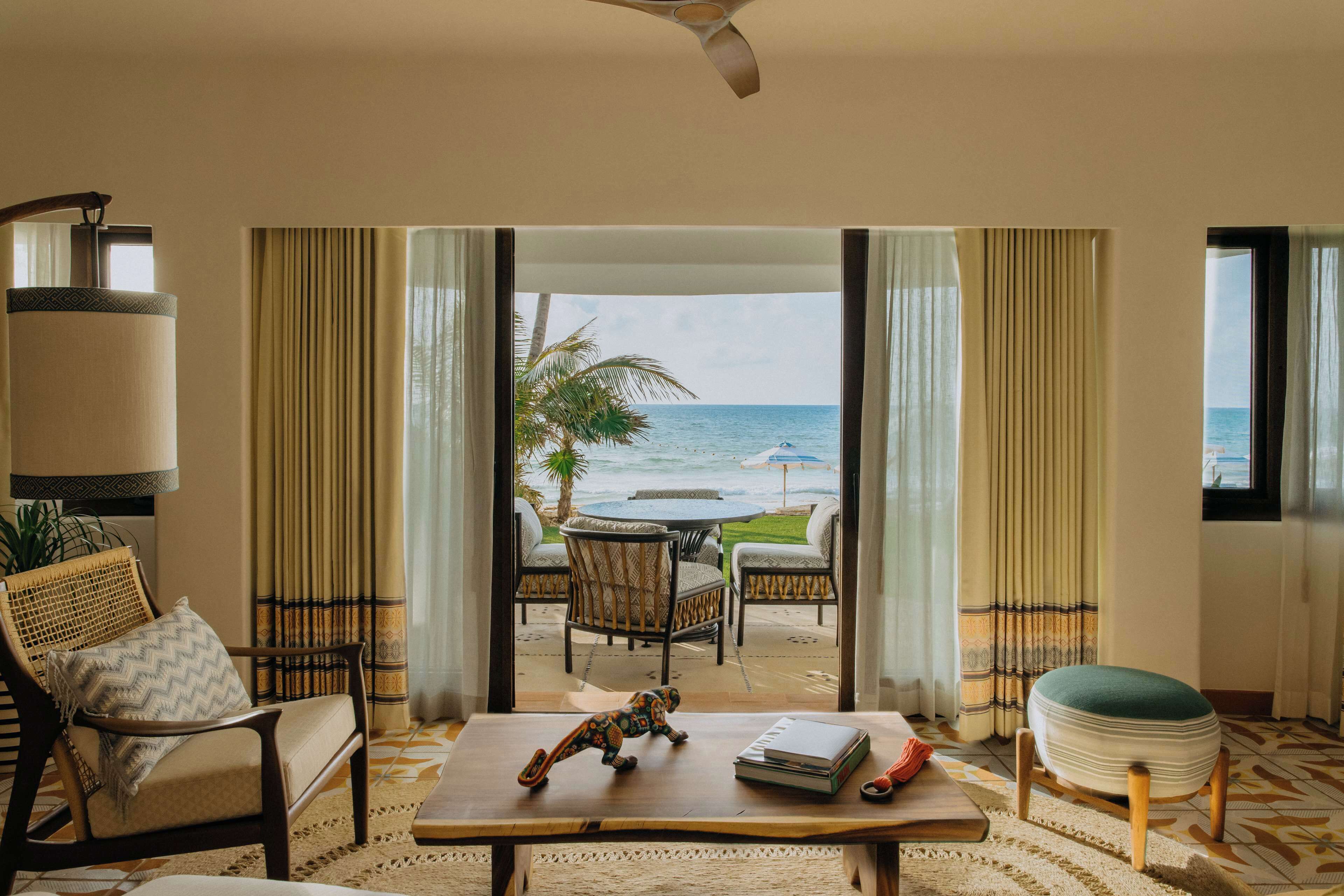 A room with a view of the ocean, a dining area with chairs and a table, and a sofa with a decorative pillow.