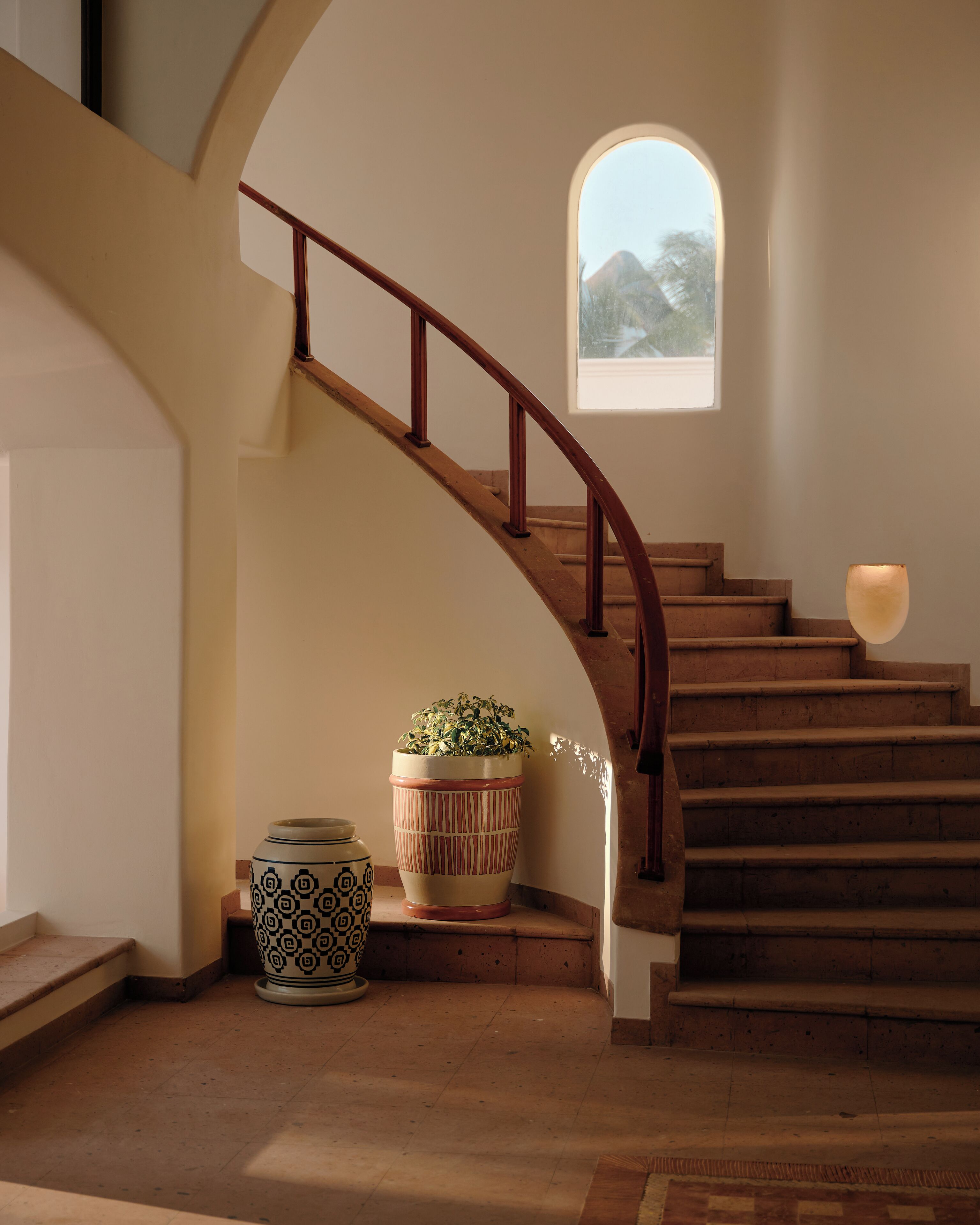 Una escalera con barandilla de madera, una planta en maceta y un florero en el rellano.