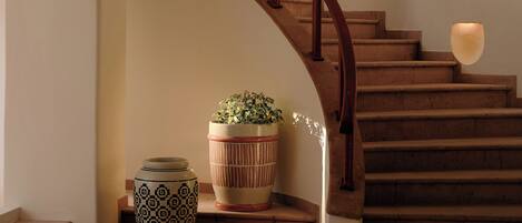 Una escalera con barandilla de madera, una planta en maceta y un florero en el rellano.