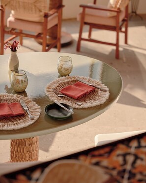 A round glass table with a woven placemat, a folded red napkin, a knife, a spoon, and a small bowl. - Maroma, A Belmond Hotel, Riviera Maya (Playa del Carmen)