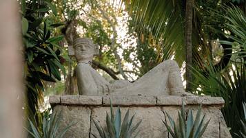 A stone statue of a reclining figure on a stone platform with plants.