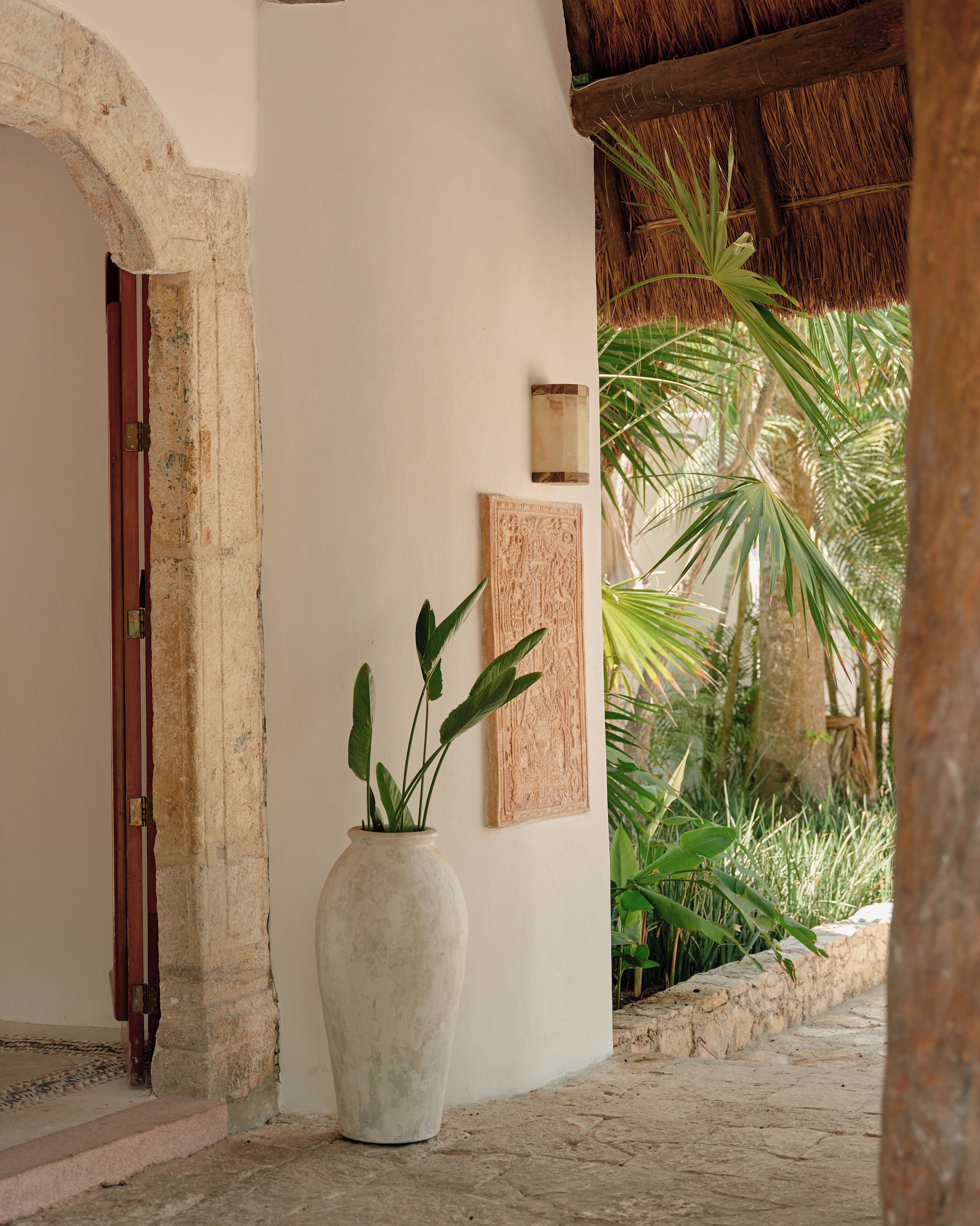 A hallway with a large white vase, a wooden door, and a framed picture on the wall.