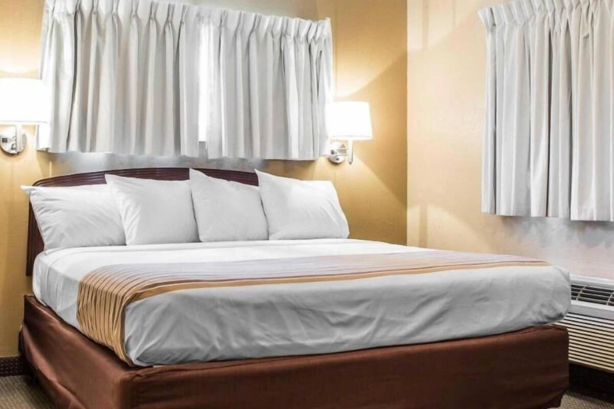 A hotel room with a bed, curtains, wall-mounted lamps, and a radiator.