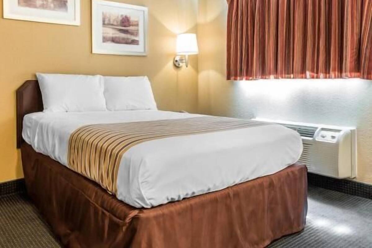 A hotel room with a bed, a wall-mounted lamp, and two framed pictures.