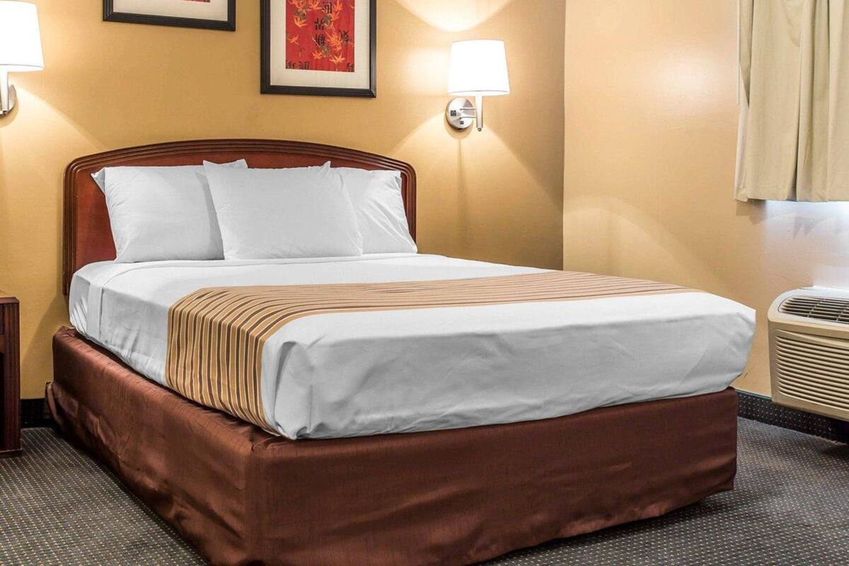 A hotel room with a bed, two wall-mounted lamps, and two framed artworks on the wall.