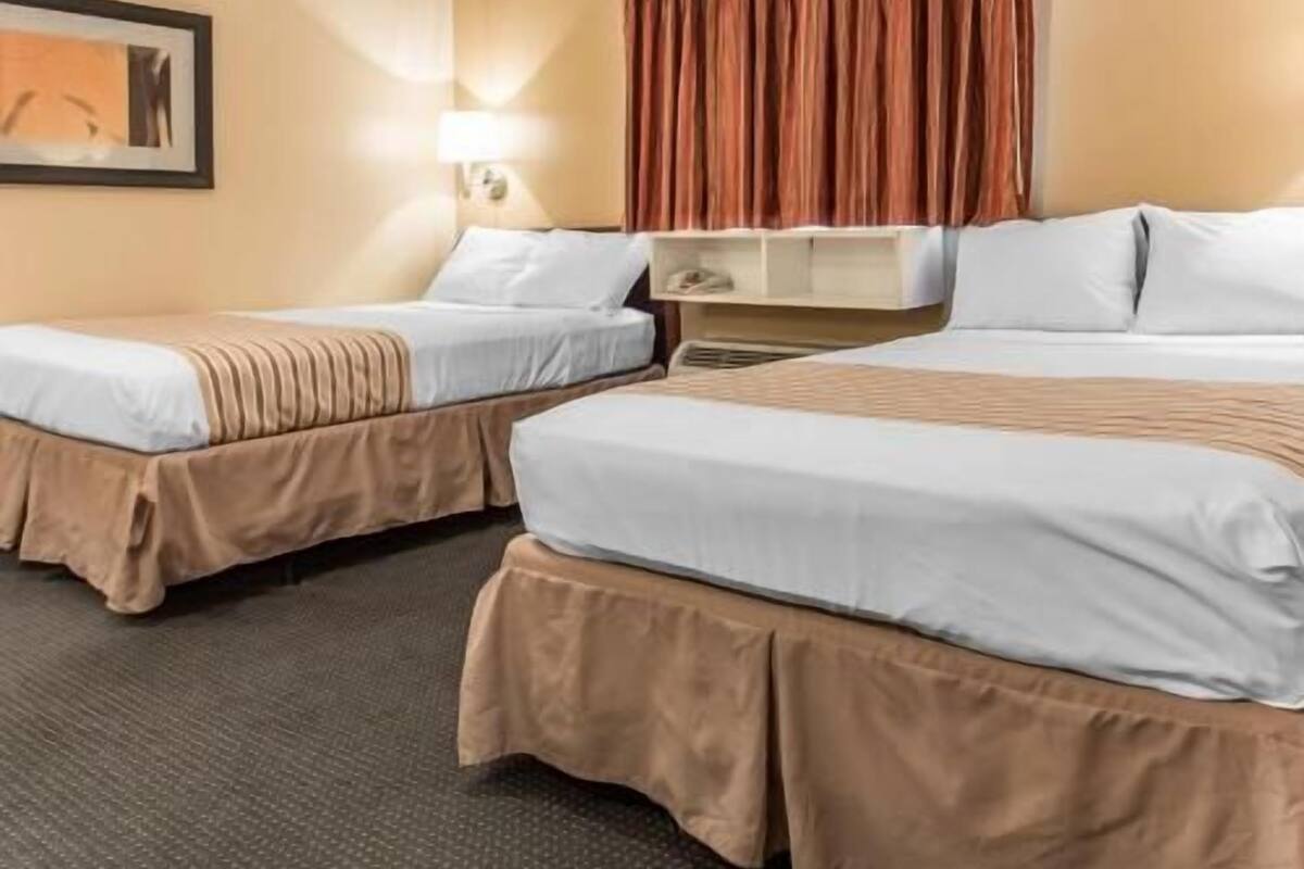 A hotel room with two beds, a desk, a lamp, and a painting on the wall.