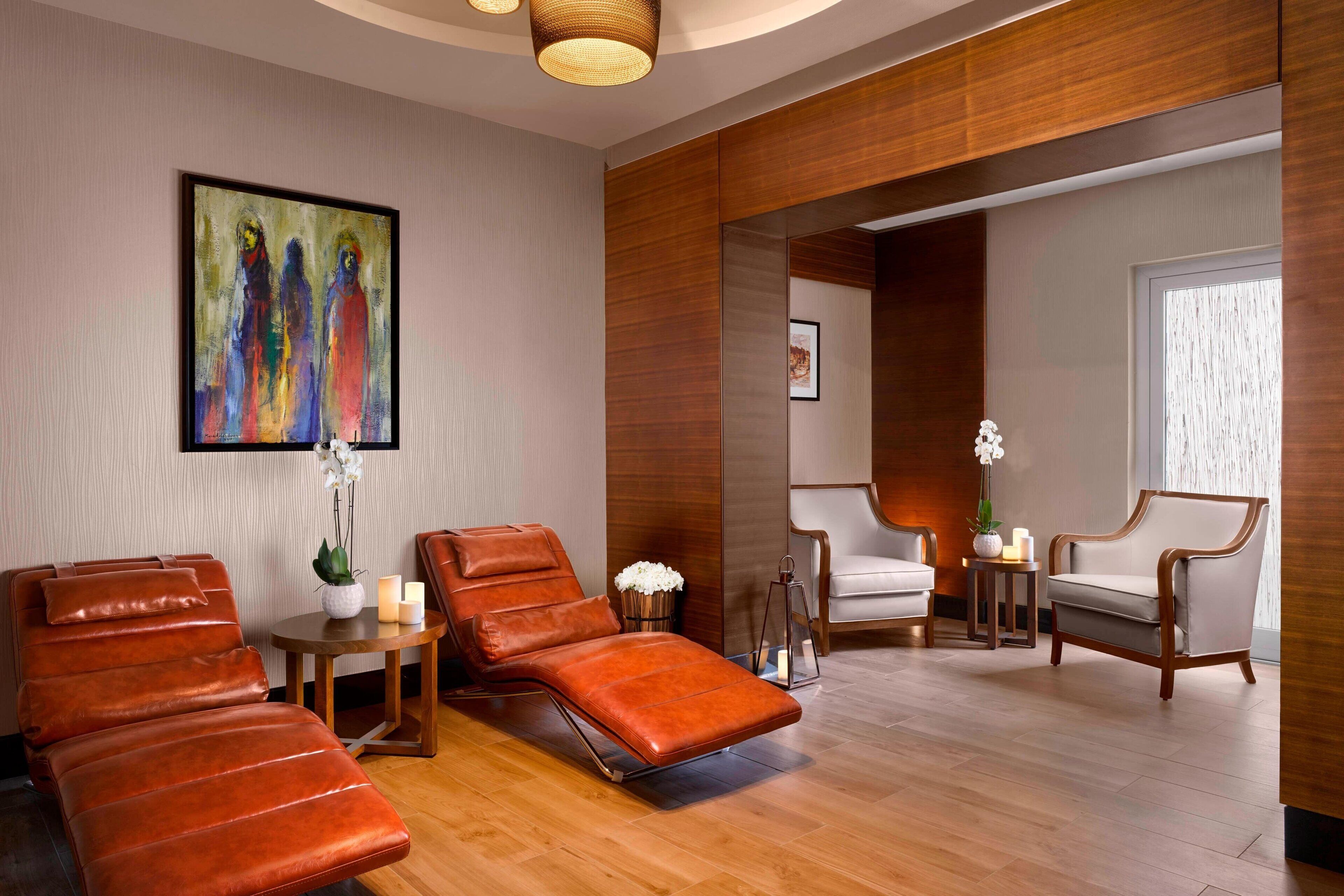 A spa room with massage chairs, a small table with candles, and a painting on the wall.