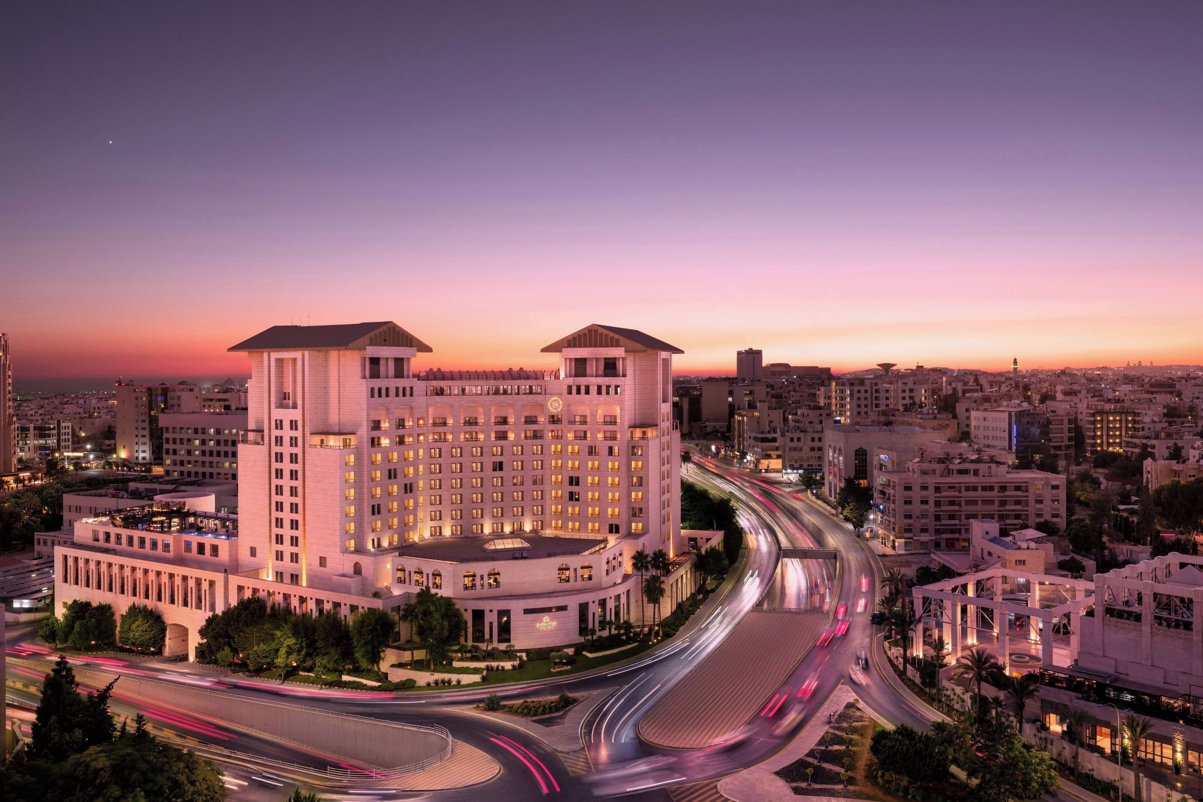 A multi-story hotel with a central courtyard, surrounded by a cityscape at dusk.