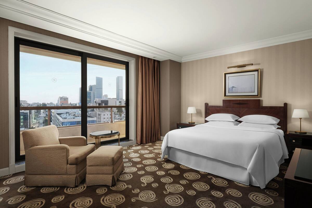 A hotel room with a large bed, a chair, a small table, and a view of the city.