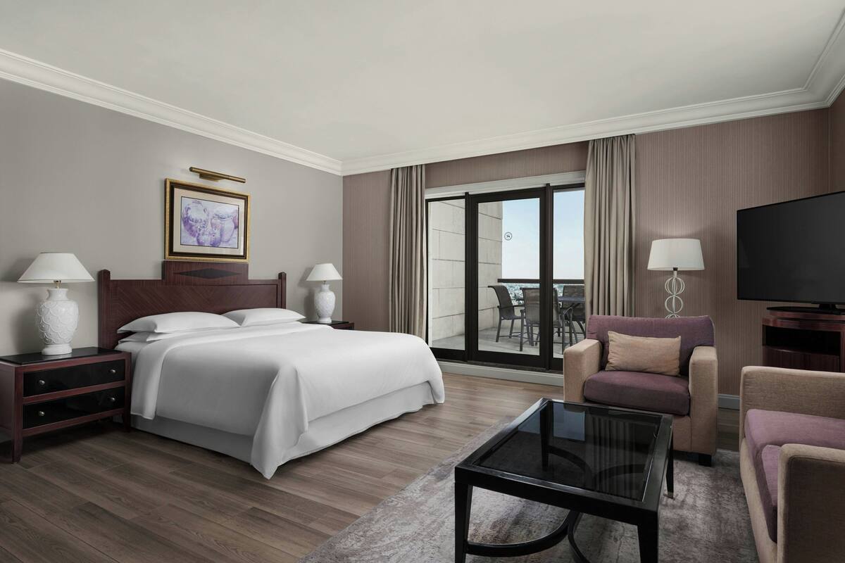 A hotel room with a bed, a sofa, a TV, and a balcony with a view.