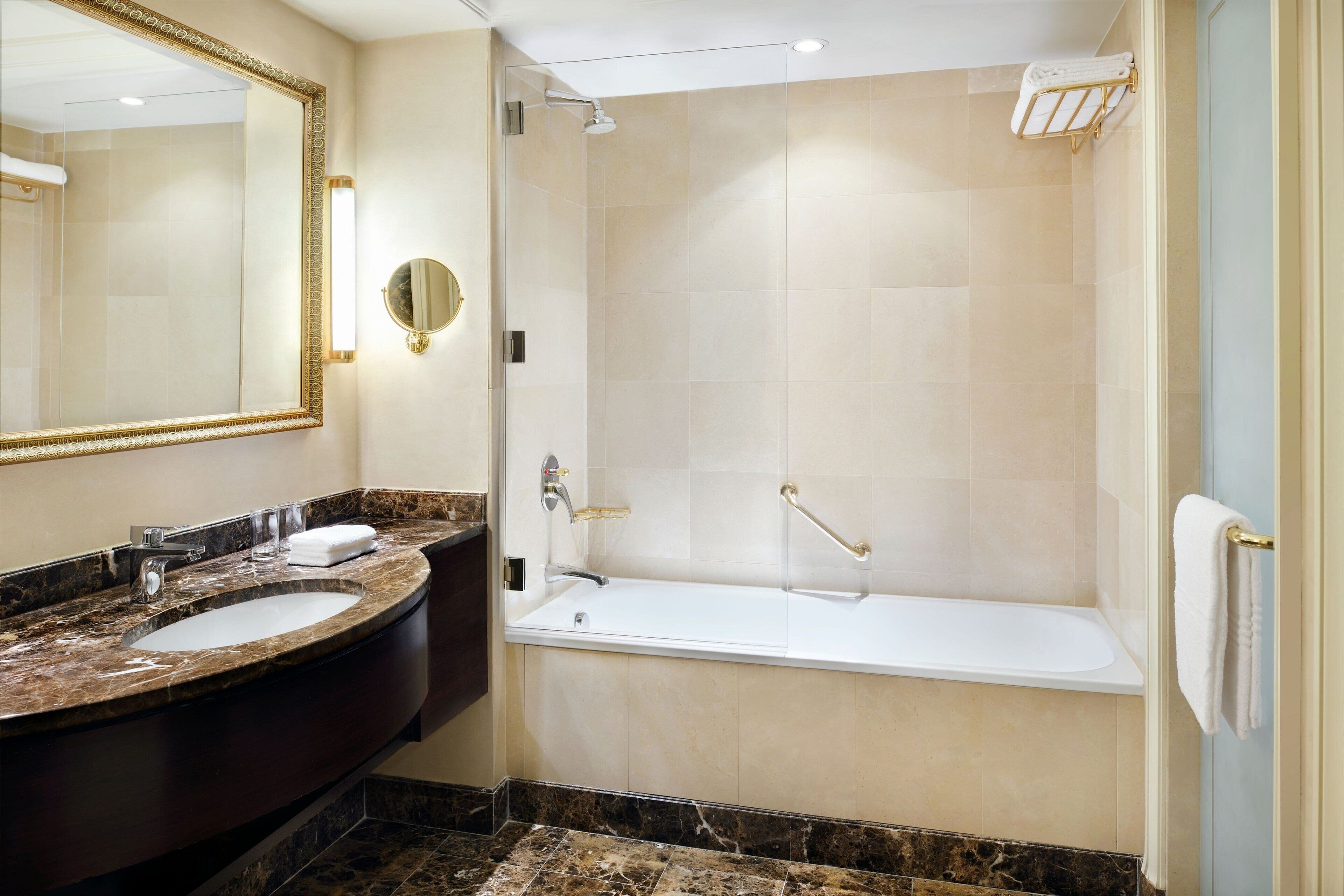 Un bagno moderno con lavabo in marmo, uno specchio grande, una vasca e una cabina doccia in vetro.