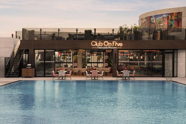Un edificio moderno con piscina, mobiliario exterior y un mural.