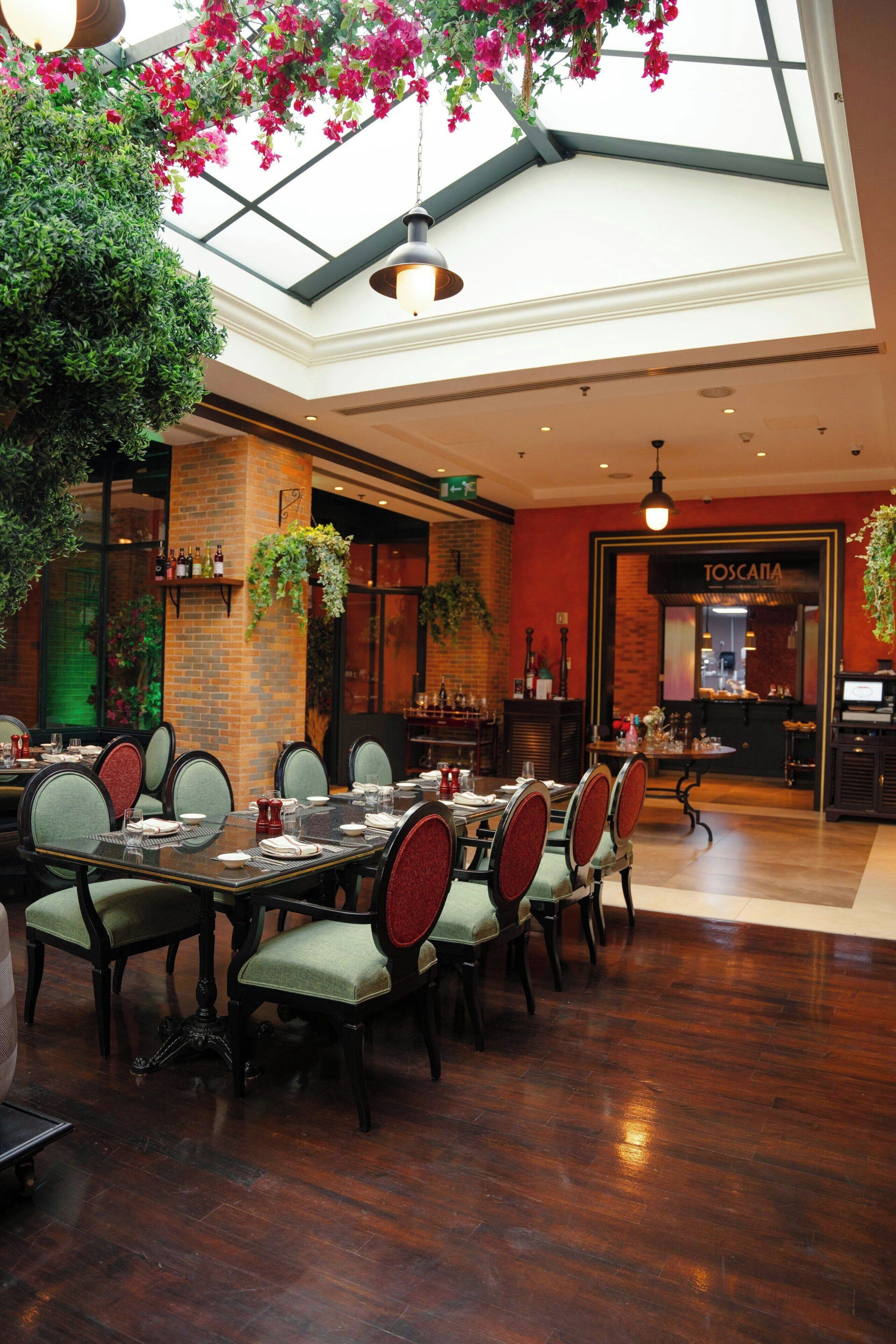 A restaurant with a high ceiling, brick walls, and hanging plants. Tables are set with chairs and dining ware.