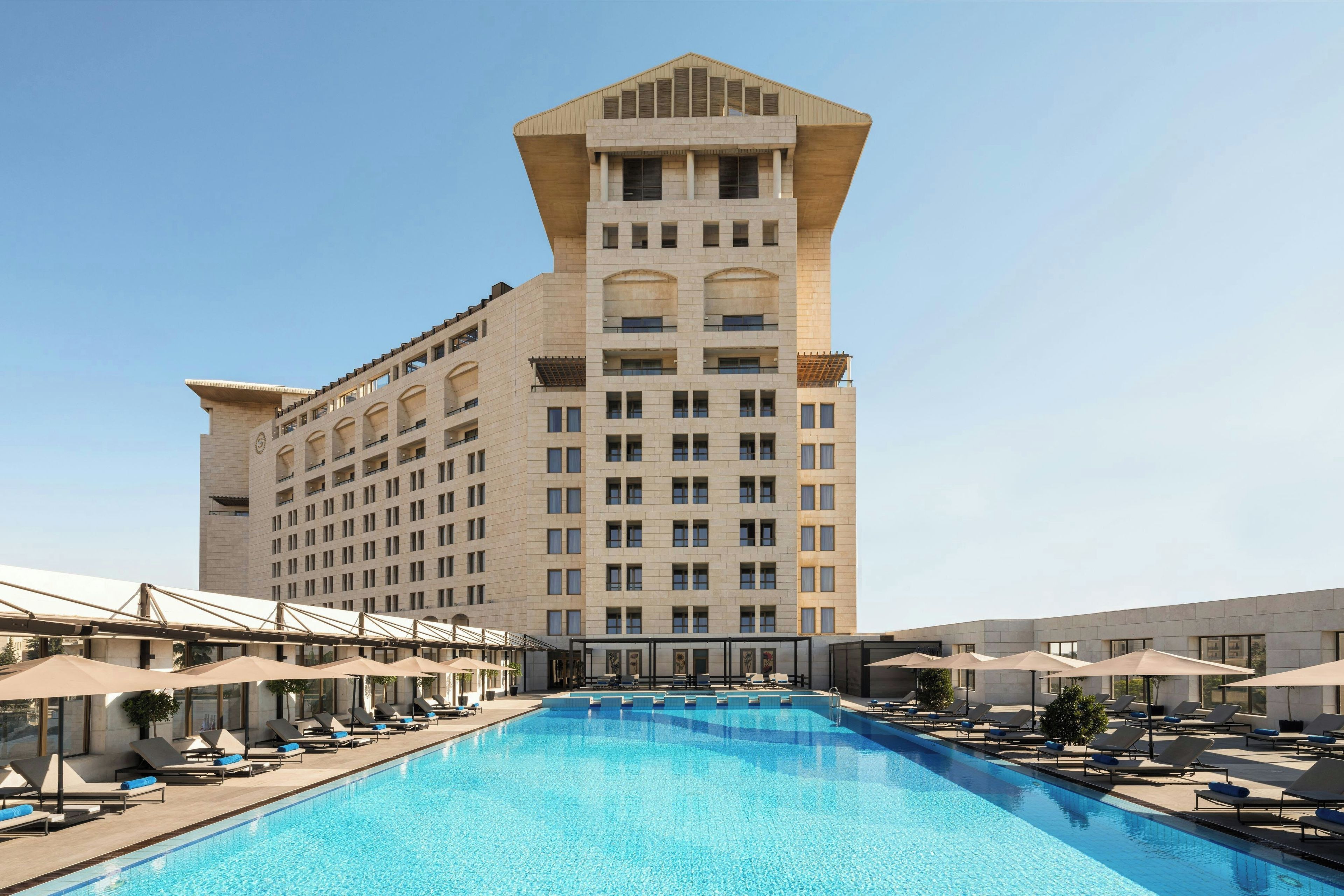 A hotel with a large pool and sun loungers.