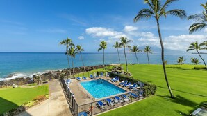 A pool area with a view of the ocean, surrounded by palm trees and blue chairs. - Kihei Surfside - Maui Condo & Home (Kihei)