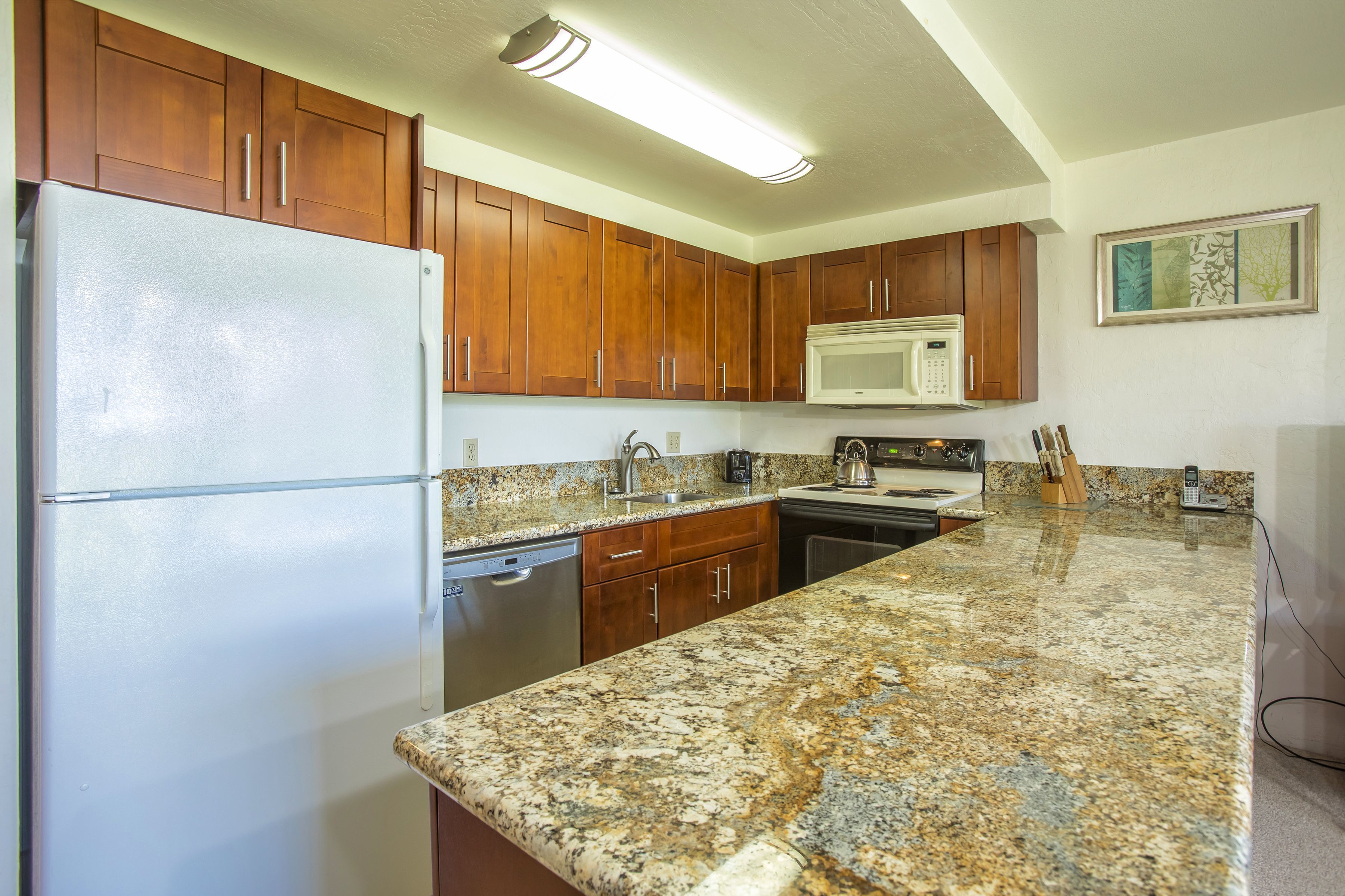 A kitchen with wooden cabinets, a white refrigerator, a microwave, granite countertops, and a dishwasher.