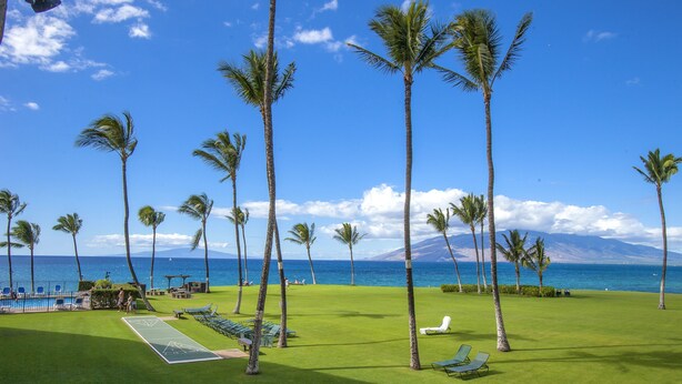A golf course with a pool, palm trees, and a view of the ocean. - Kihei Surfside - Maui Condo & Home (Kihei)