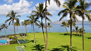 A golf course with a pool, palm trees, and a view of the ocean. - Kihei Surfside - Maui Condo & Home (Kihei)