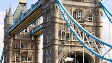 A historic stone tower with a large archway, a bridge with blue railings, and a flag on top.