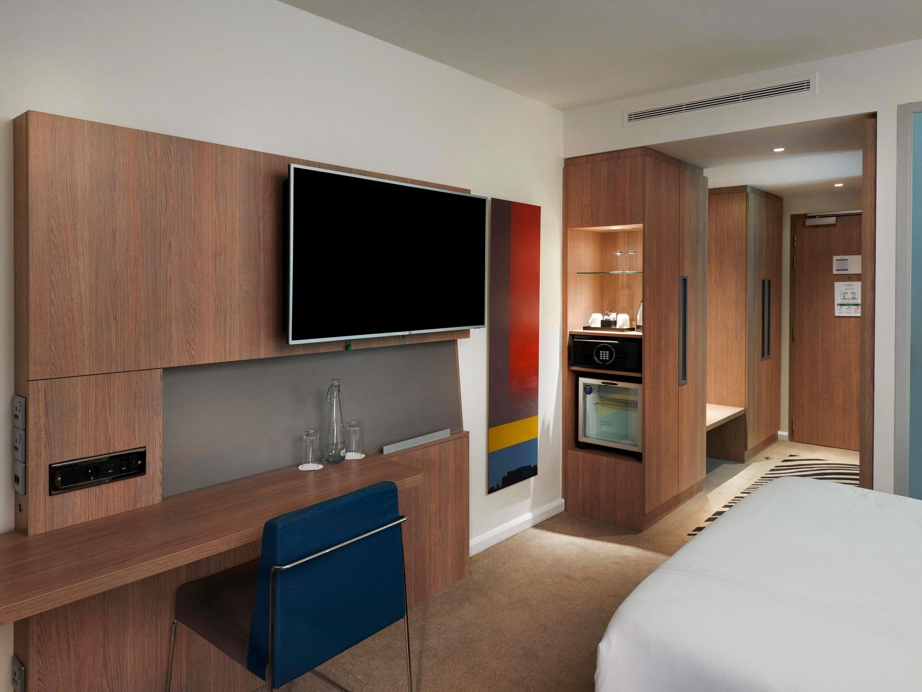 Hotelværelse med træskrivebord, fladskærms-tv, minibar, seng og badeværelse med bruser.