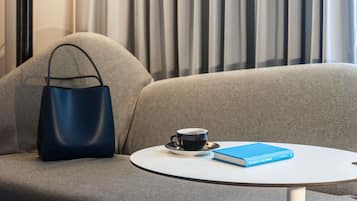 A modern room with a grey sofa, a blue handbag, a white table with a book and a cup of coffee.